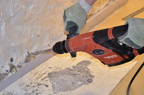 Un artisan menuisier travaille dans un atelier intérieur, assemblant une structure triangulaire en bois massif sur sol béton