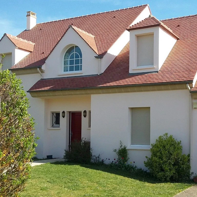 Façade de maison résidentielle avec toiture en tuiles terre cuite et lucarnes à bardage blanc